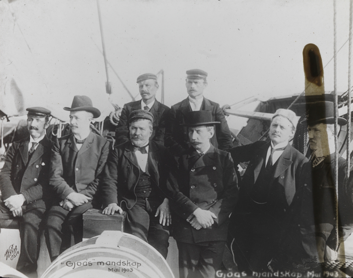 Håndkolorert dias. Gruppeportrett av mannskapet på Gjøa. Sommeren 1903 seilte Roald Amundsen ut fra Oslo med skuta Gjøa. Målet for ekspedisjonen var Nordvest-passasjen.