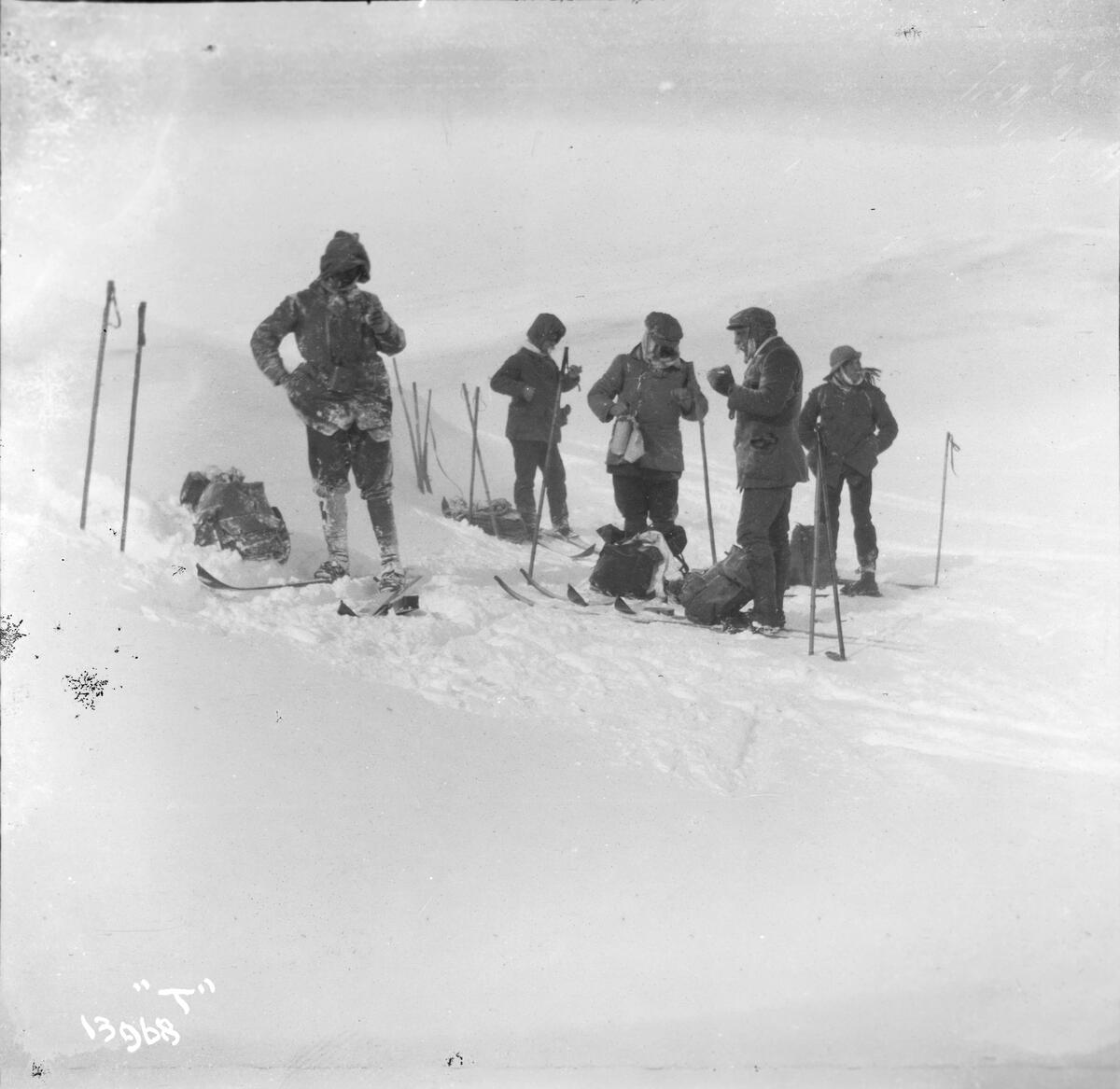 Fem menn på ski tar en pause i et snødekket landskap.