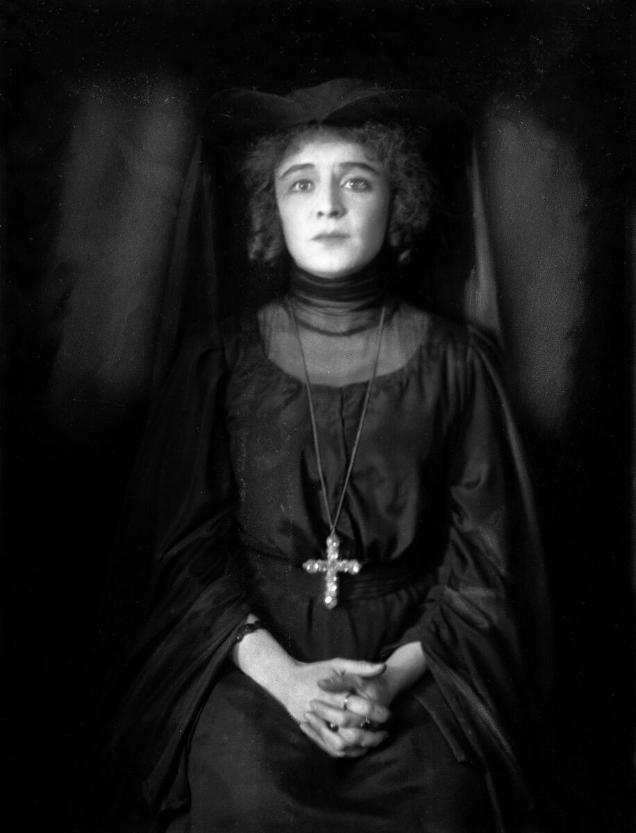 Portrett av skuespilleren og sceneinstruktøren Gerda Ring. Hun poserer i en svart kjole og en vid hodebekledning. På brystet bærer hun et korskjede.