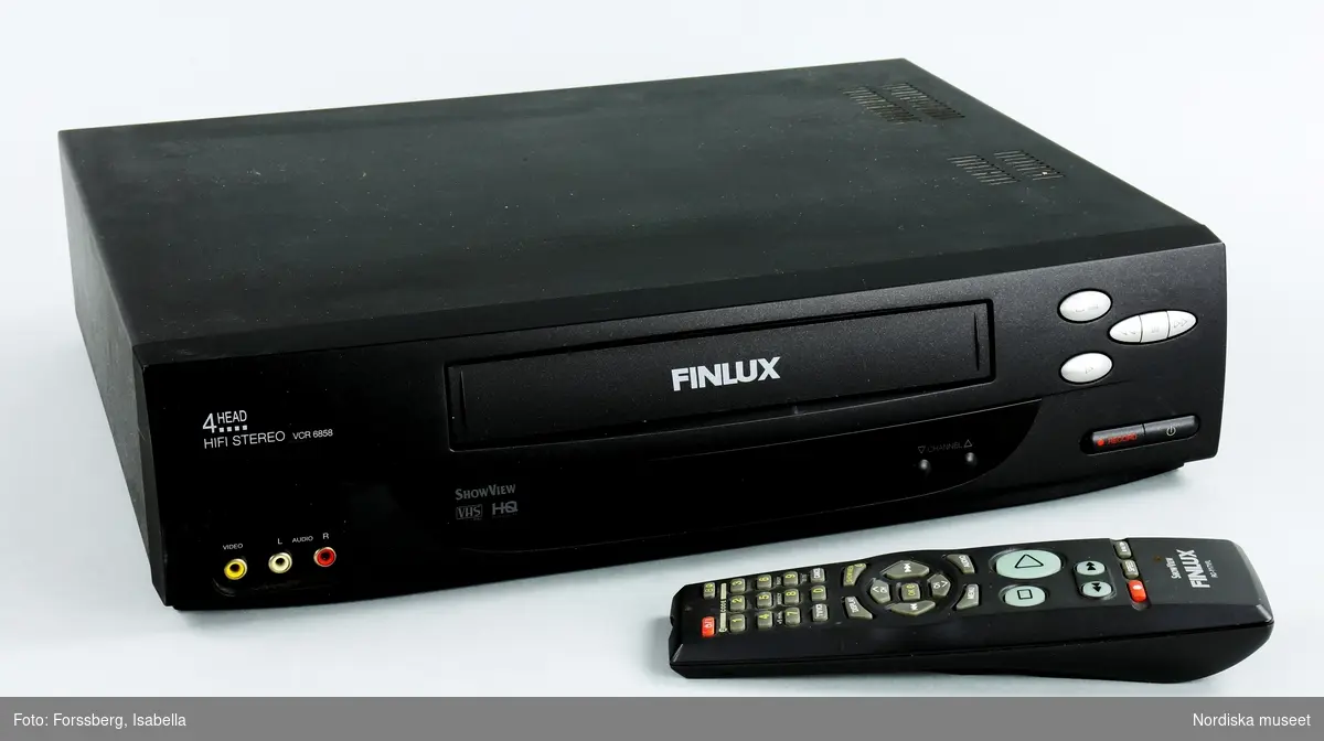 a) Svart VHS spelare (videbandspelare) med b) fjärrkontroll, 
c) förbindelsekabel mellan VHS-spelare och TV och 
d) anslutningssladd till eluttag samt e) bruksanvisningl.