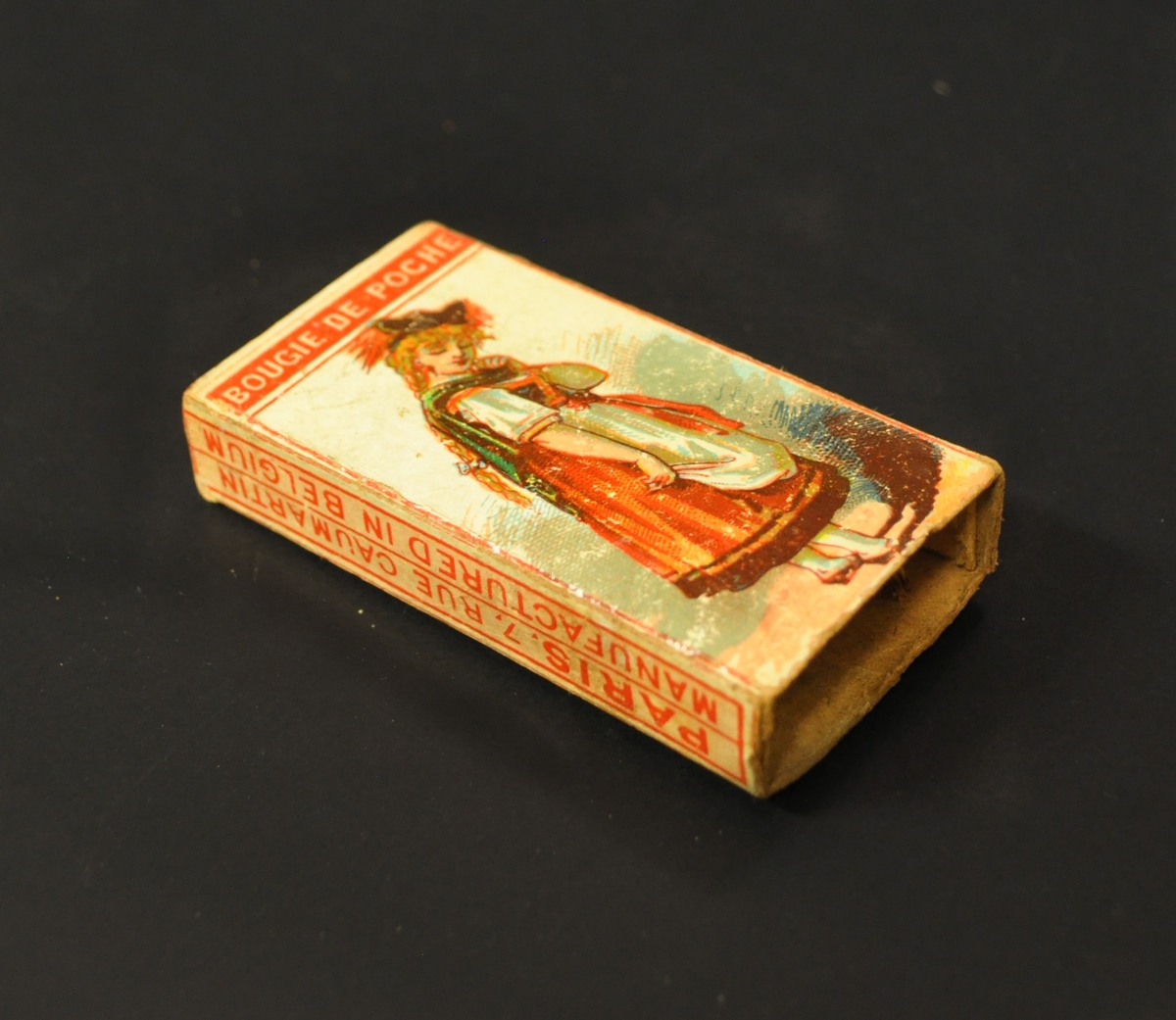 Tändsticksask som innehåller ett antal vaxtändstickor. Motiv på asken: en kvinna i folkdräkt.