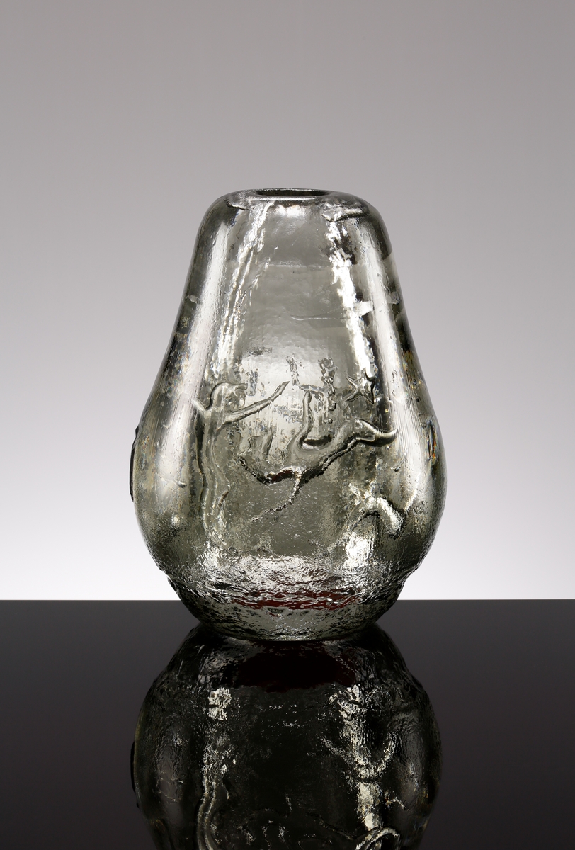 Formgiven av Edvin Öhrström. Arielvas, päronformad i ljusgrått glas. Dekor bestående av abstrakt luftmönster förställande Neptunus, sjöjungfrur och fiskar. Vasens utsida reliefmönstrad.