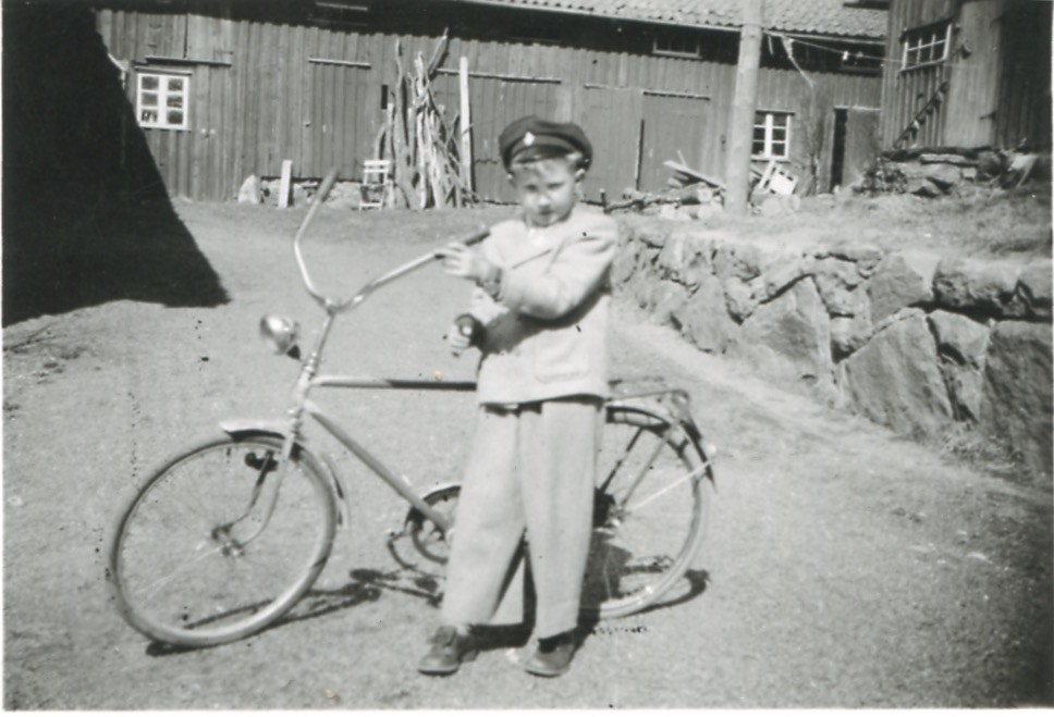 Kållered Stom "Nygård" cirka 1955. Lars Johansson (född 1945) står med sin cykel på gårdsplanen. Ladugården ses i bakgrunden.