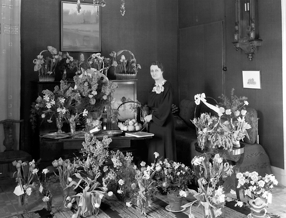 Kvinna med fruktkorg omgiven av blommor.
Fotografens ant: Fröken Svea Andersson. 1936.