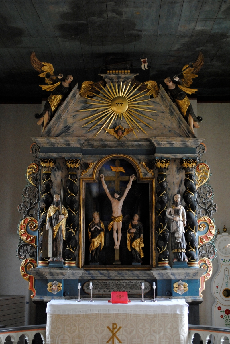 Interiör i Laxarby kyrka. Altaruppsatsen är från 1769 och centralmotivet består av en så kallad kalvariegrupp med Kristus på korset omgiven av Maria och aposteln Johannes. Uppsatsen, liksom predikstolen från 1747, två änglar med psalmnummertavlor från 1767, och en timglasängel, är alla utförda av den i stiftet välkände bildsnidaren Isak Schullström. Taket dekorerades 1777 med moln och stjärnor av kyrkomålaren Carl Zetterström.
