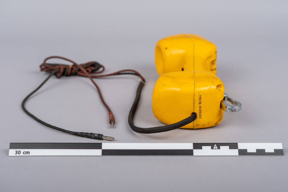 Gul Prøvetelefon fra Tele
Type: Prøvetelefon TS21-N

Prøvetelefonen består av et telefonrør og kabel som åpner seg i 2 linjer, en rød og en svart.

På innsiden av håndsettet øverst og nederst 1-1 svarte runde trykknapper, i midten vippebryter for av/på.

Oversiden av håndsettet har tastatur av tall (0-9), stjerne, nummertegn og bryter til kontrollfunskjon. 
Nederst metall karabinkrokk.
Bruksmerker på overflaten.