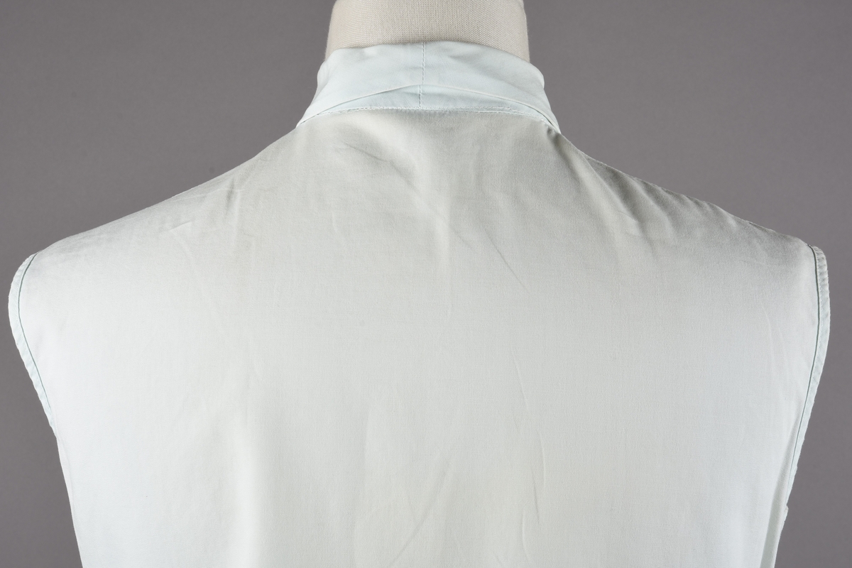 Ermeløs bluse av bomull. Blusen er kneppet i front med fem knapper i plast.
