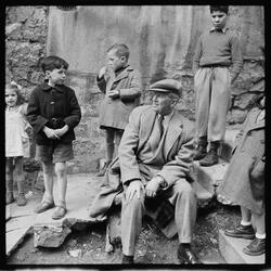 Maurice Chevalier sitter på en trapp, rundt han står tre gut