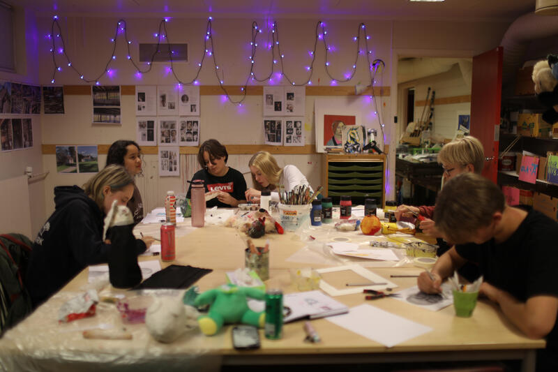 Elever sitter rundt et bord. De maler, tegner og lager skulpturer.
