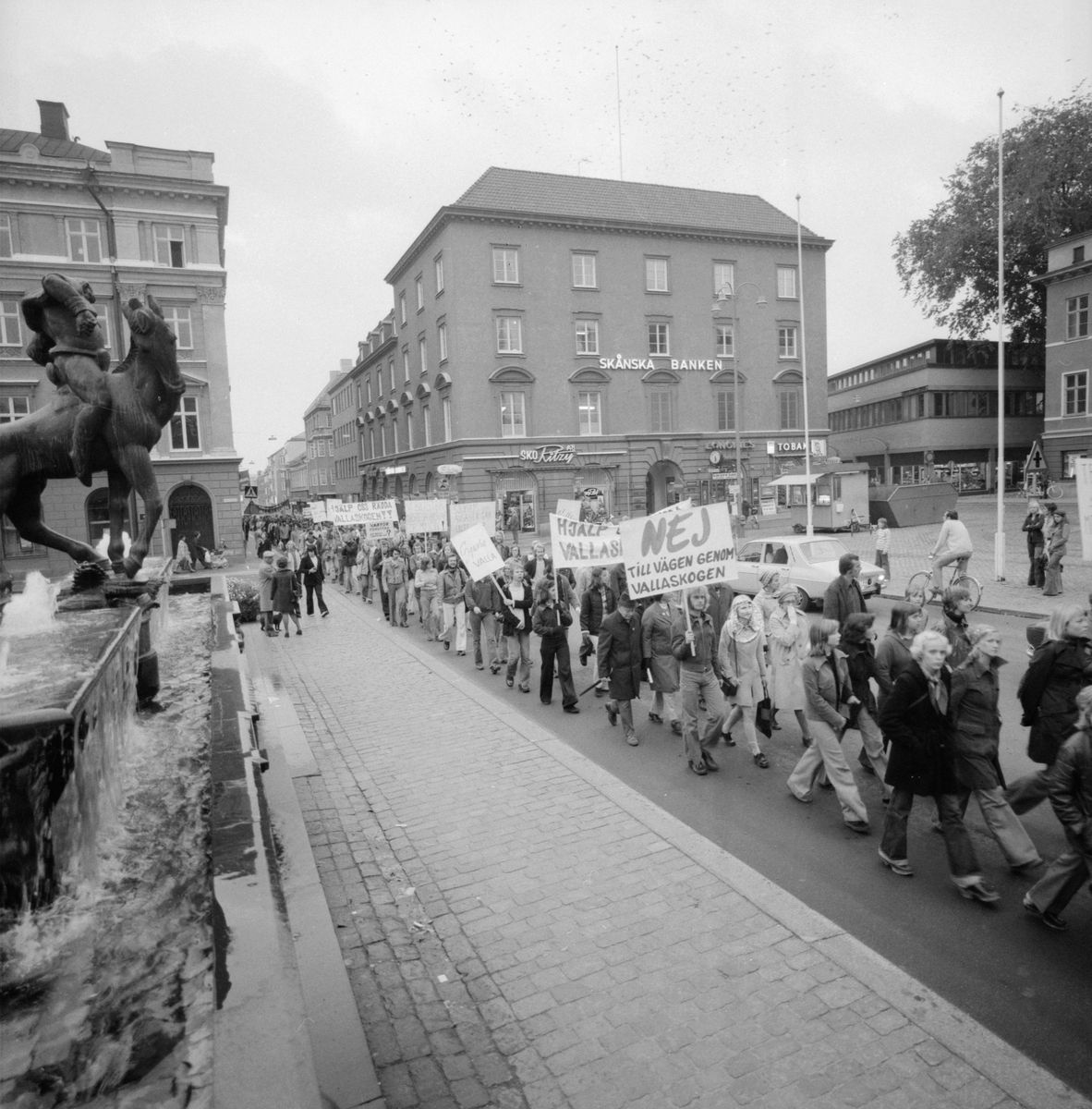 Planer på en trafikled genom Vallaskogen skapade stor debatt under främst 70- och 80-talen. Redan under 1950-talet hade idén om en ringled i Linköping framkommit och från 1968 var delar inritade i stadens generelplan. Torgmöten blev en vanlig syn, liksom stora demonstrationer tills en kommunal folkomröstning satte punkt i frågan 1989. Här passerar att av många demonstratonståg Stora torget. Just detta hösten 1974.