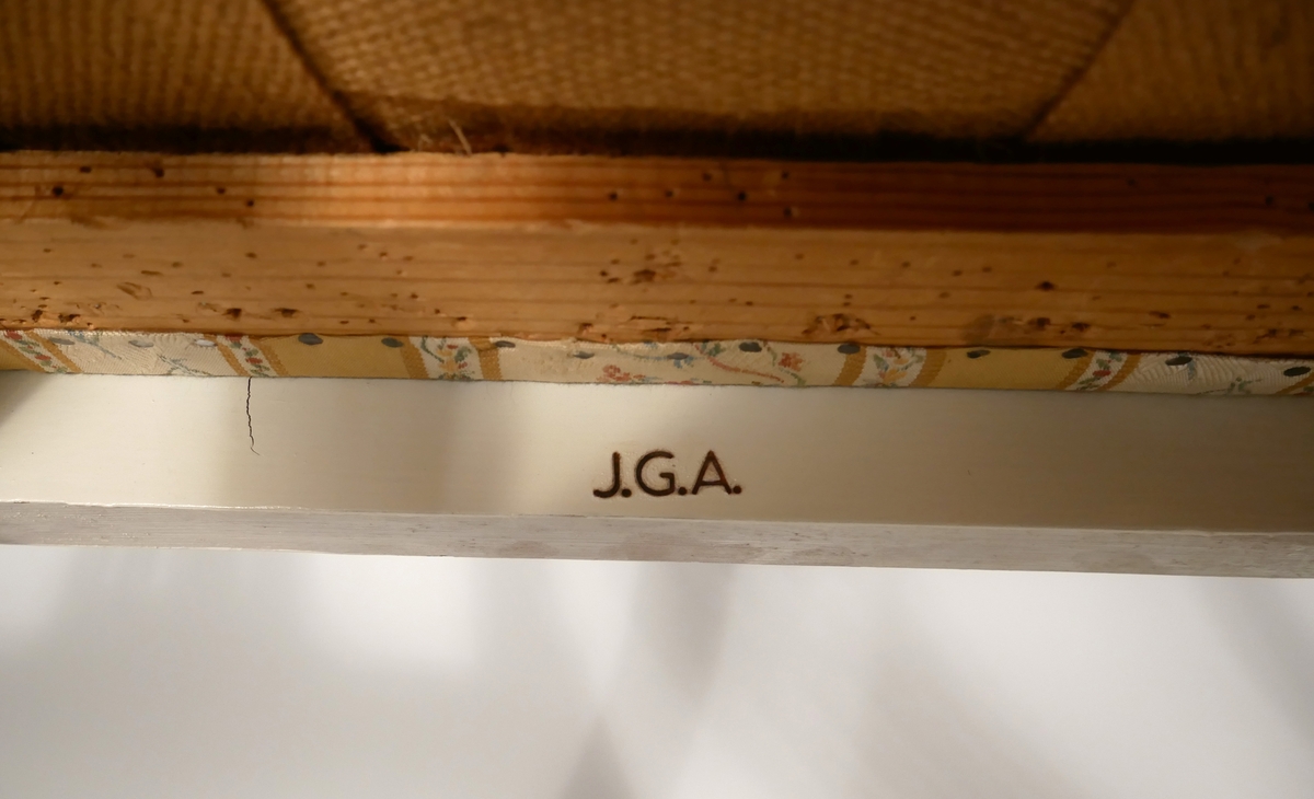 Två vitmålade stolar med löstagbar klädd sits. Märkta J.G.A. = J.G. Axelssons snickeriverkstad. Verkstaden tillverkade möbler på beställning och efter kundens önskemål.