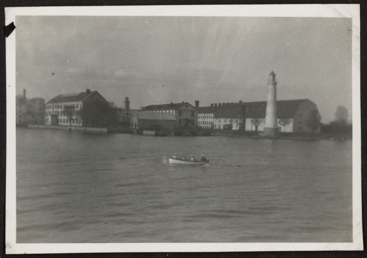 Bilden föreställer en vy på Stumholmen från havet. I förgrunden befinner sig en roddbåt med sjömän.