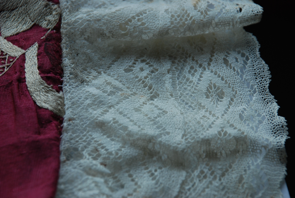 Dåpspose i burgunder silkerips med hvite blonder langs kantene og kremhvit silkebroderi.