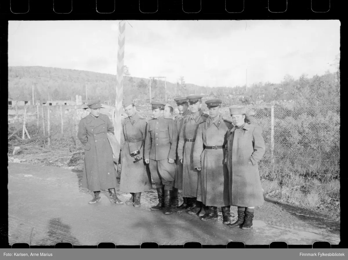 En gruppering russiske soldater poserer for et foto på grensa i Sør-Varanger ved grensebom i Storskog.  

Mann som er nr. 2 fra venstre har et kamera festet til belte 

Helt til høyre kan man se en kvinne som antagelig tilhørte det Sovjet-russiske militæret 