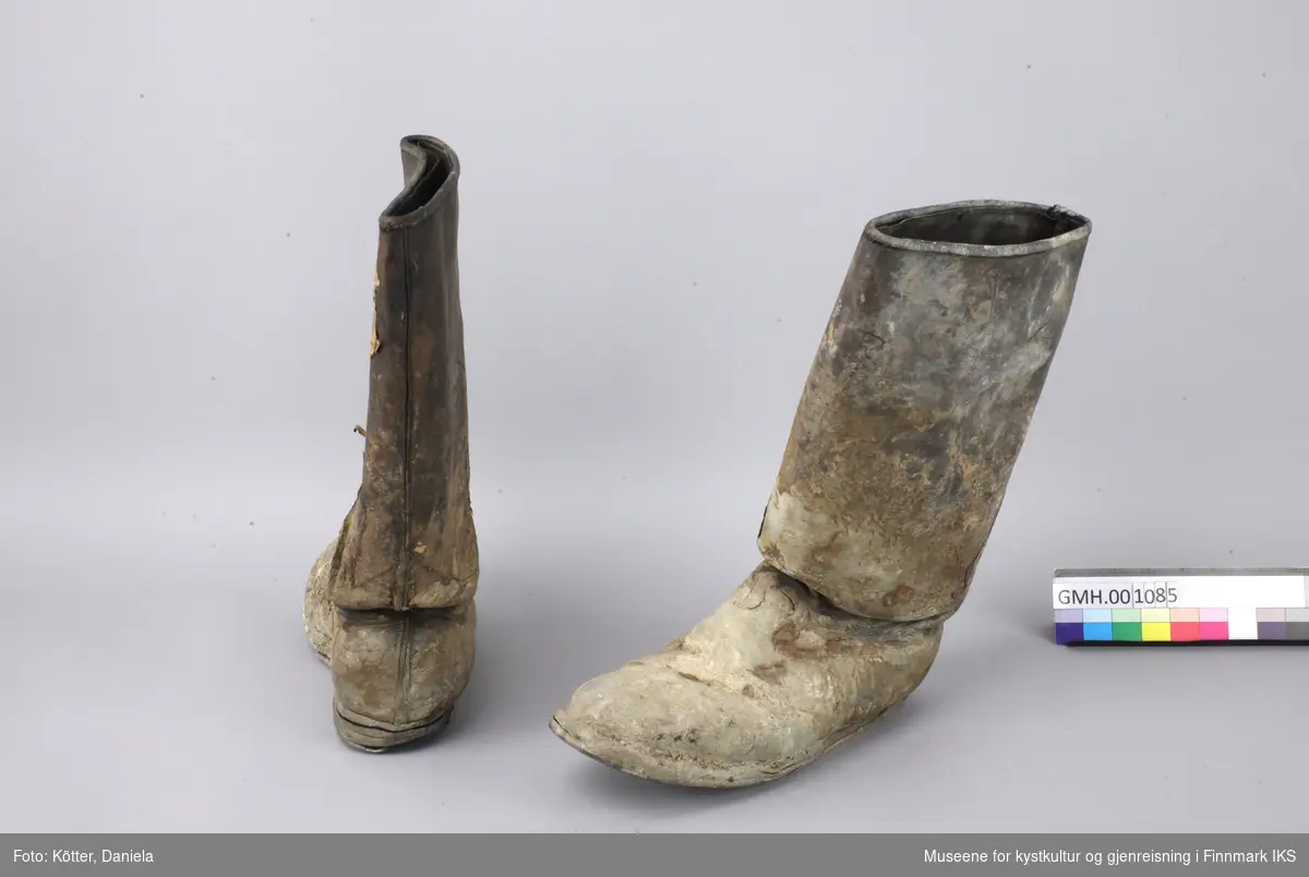 Ett par brune lærstøvler med høye skaft, som helt tydelig ble brukt til arbeid. Sålene er festet med spikre. Støvlene er i herrestørrelse og forurenset med mørtel og papir. 