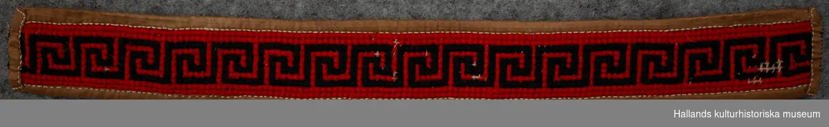 Strumpeband med korsstygnsbroderi med meandermönster, svart på röd botten, ljusbrunt sidenfoder.