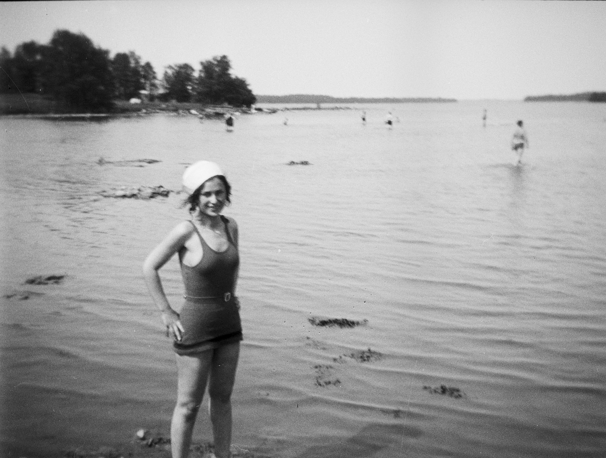 En kvinna i baddräkt står i vattnet vid badstrand, Gräddö, Uppland
