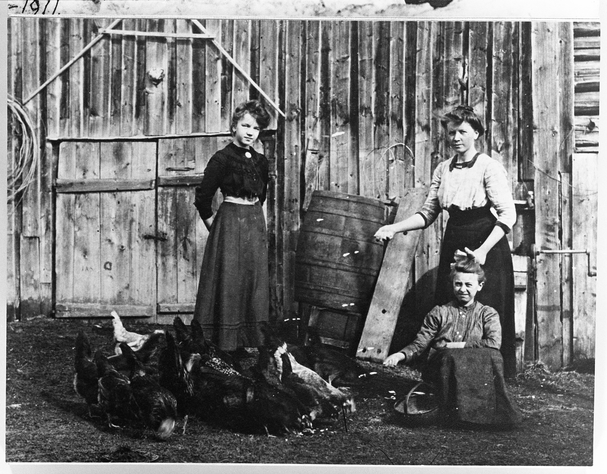 Anna og Marie Skinderviken står, mens Astrid (Johans datter) sitter foran en låvevegg. April 1911.