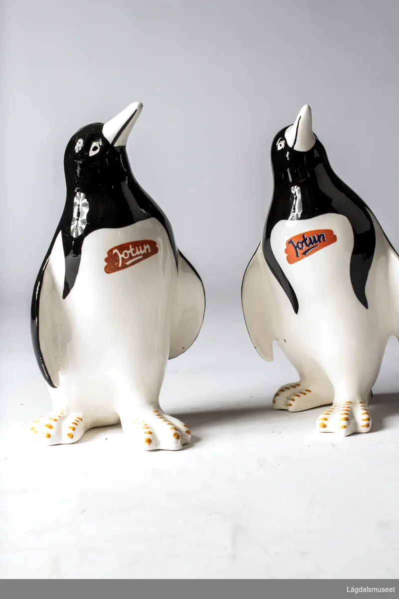 Pingvin i fajanse med firmalogo for Jotun i blå bokstaver på oransje bakgrunn på brystet til pingvinen.