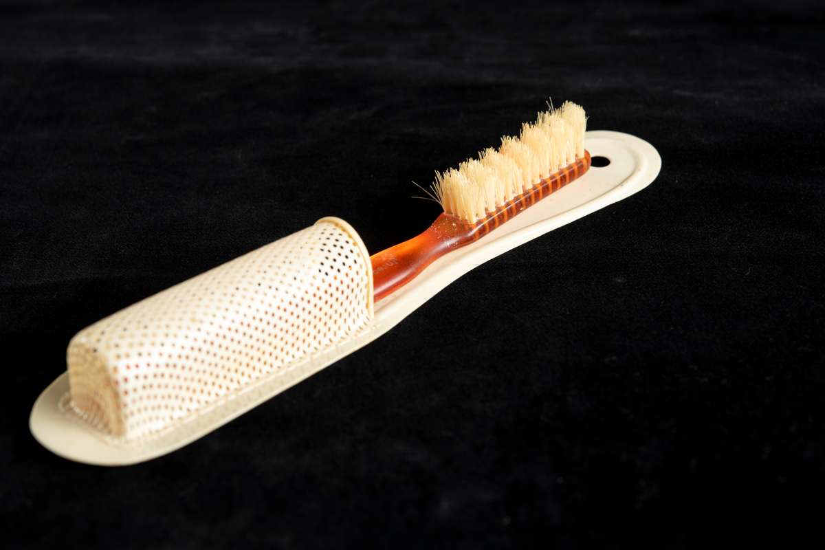 Rödbrun/orange tandborste med tillhörande vit hållare.