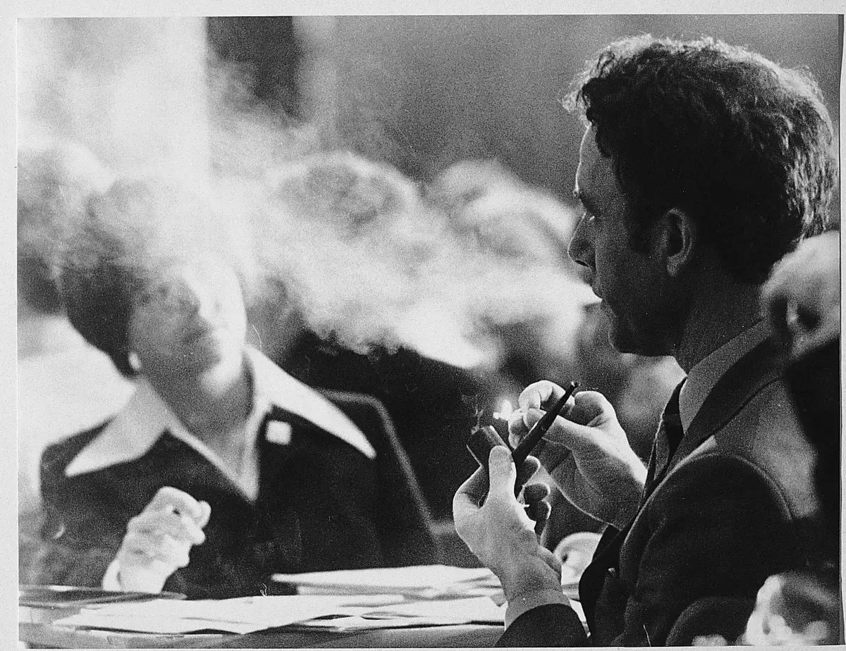 Bilde av Reiulf Steen som sitter og røyker pipe, på den andre siden av bordet sitter Gro Harlem Brundtland innhyllet i piperøyk.