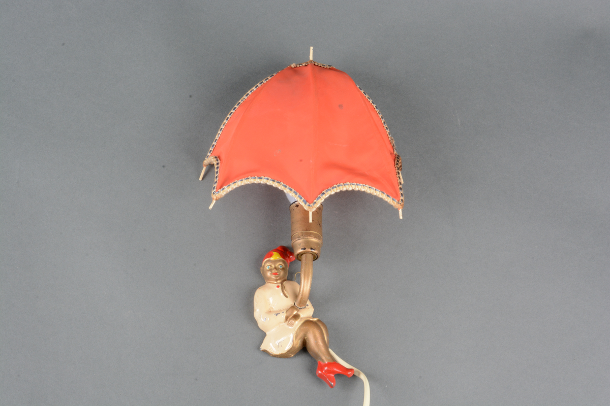 Lampe til å montere på vegg. Lampen (A) er montert på en metallbase som er formet som Ole Lukkøye kledd i nattkjortel, tøfler og nattlue. Ledning uten støpsel. Tilhørende lampeskjerm (B) med kunstfiber og med metallfeste bak. Lampeskjermen er formet som en paraply. Possement rundt kantene på paraplyen.