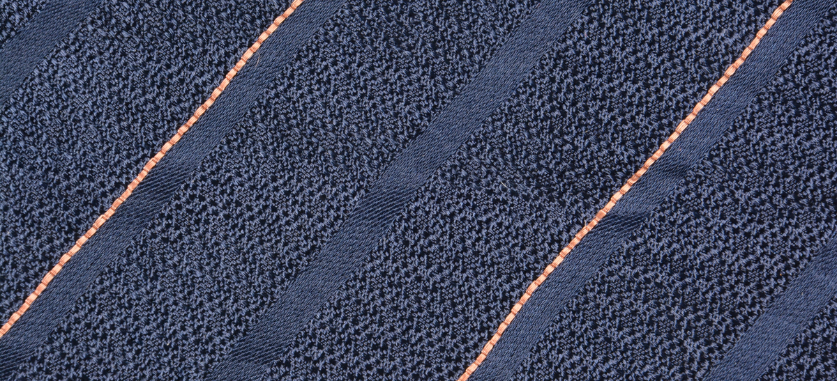 Slips av kunstfiber med mørkeblått skall (konvolutt) med oransje og svart-stripet mønster. Ikke noe fôr. Rem bak for å feste slipset i ved bruk. 45 graders søm på bakstykket hvor delene er sydd sammen.