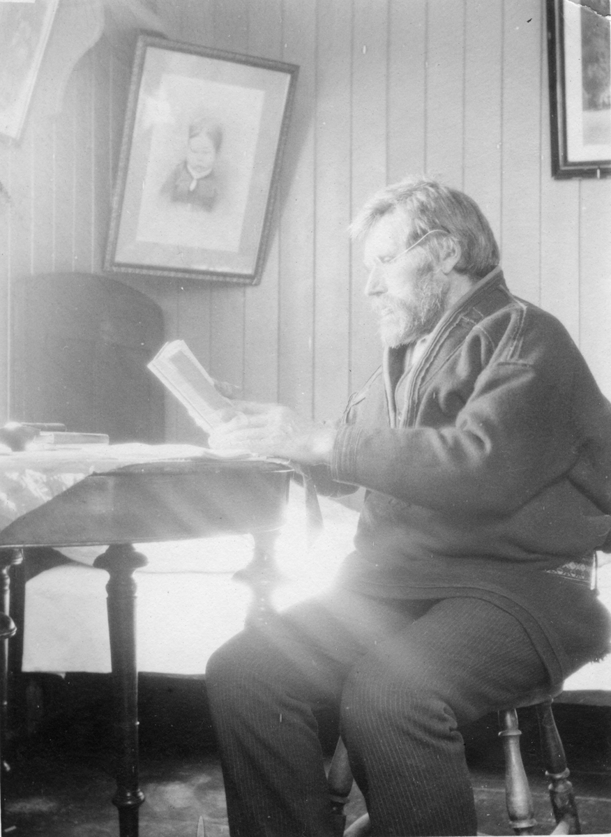 En mann i samisk kofte sitter ved et bord og leser