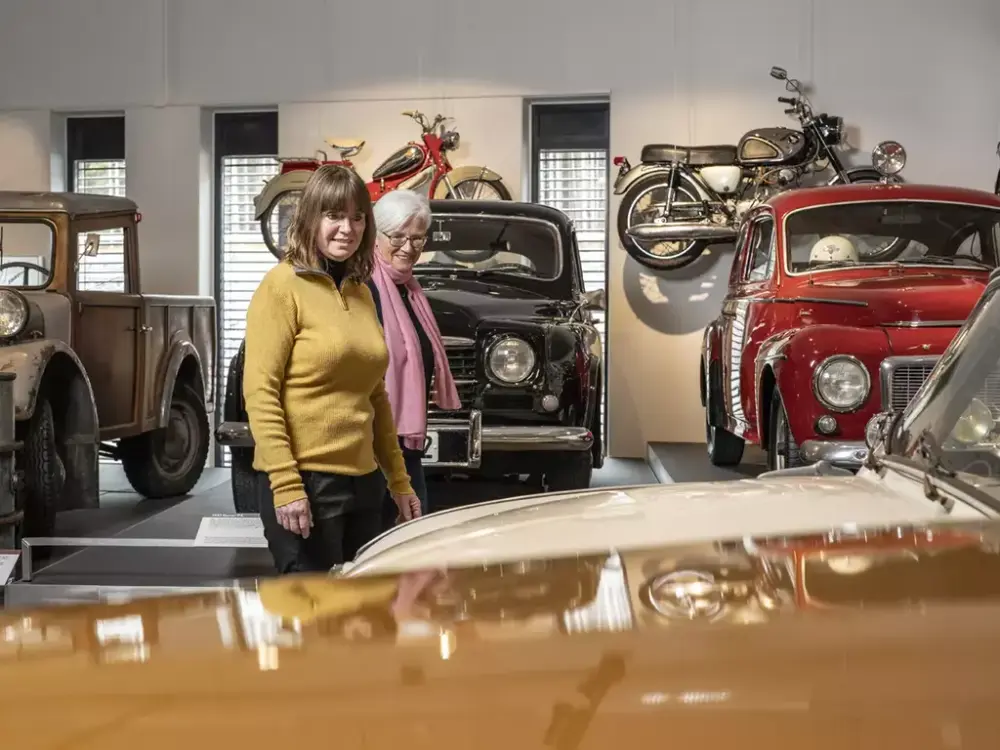 Bildet viser to personer som ser på en bil på Norsk kjøretøyhistorisk museum.