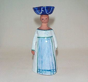 Figur av lergods, föreställande en kvinna med vit fotsid klänning och ljusblått förkläde med mörkblå dekor. På huvudet bär hon ett mörkblått kar.