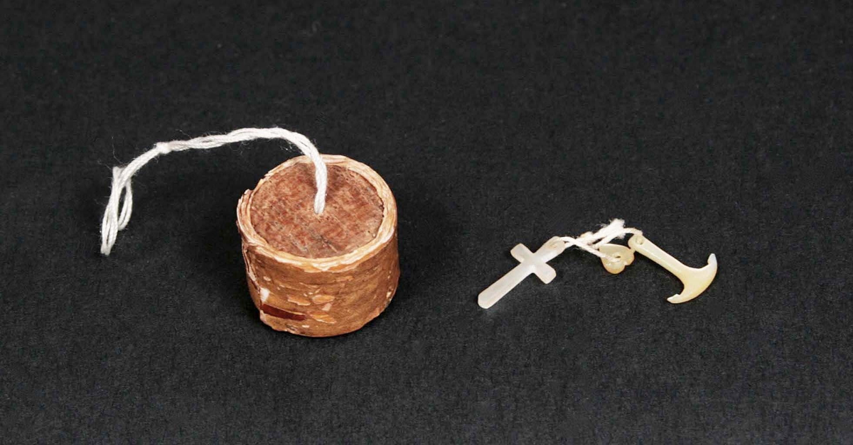 Rund ask med löst lock av trä. I asken förvaras kors och ankare i pärlemor.