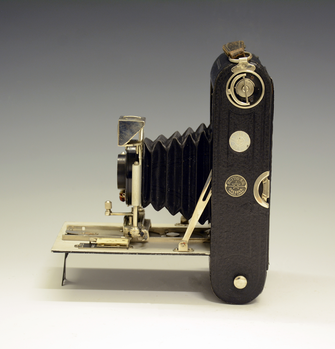 Kamera sammenfoldet i sort, flat, rektang. kasse m/bærehank. Modell 1908, H. Abel, Christiania (forhandler).