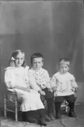 Studioportrett av en pike og to gutter som sitter på hver si