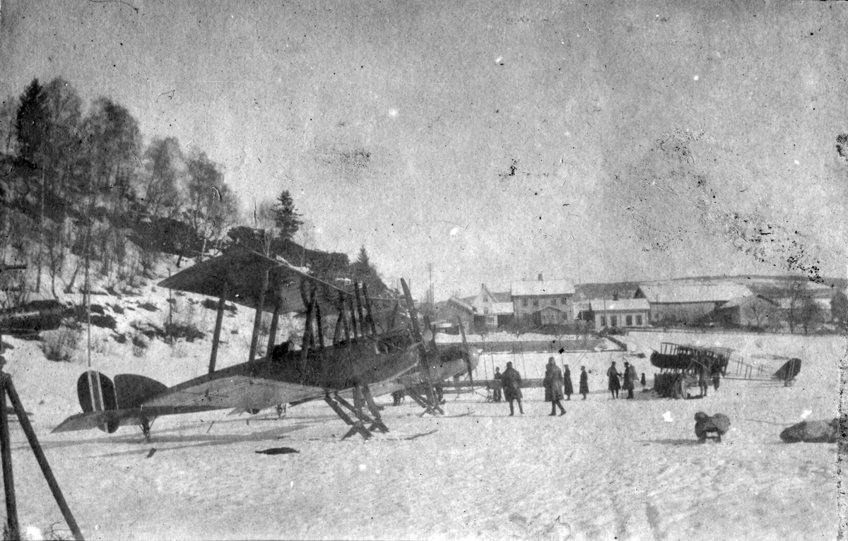Fly og flygere oppstil på den islagte Mjøsa under Hærens flyvesens vinterøvelse på Lillehammer i 1920. Nærmest et britisk rekognoseringsfly av typen BE 2E og lengst til høyre en Farman Shorthorn. Det kan være Vingnes gård som ses i bakgrunnen.