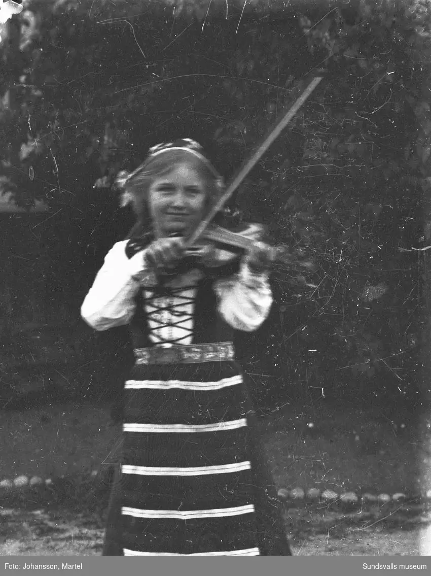 Ester Åberg, Alnö, spelar fiol iklädd folkdräkt. Ester spelade i Gustafsbergs barnorkester som leddes av folkskolläraren Henrik Samuelsson (samma grupp som operasångerskan Hjördis Schymberg var med i). Ester var kusin till fotografen och hans syskon.
