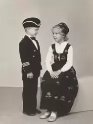 En liten gutt og jente i bunad og drakt som ser på hverandre