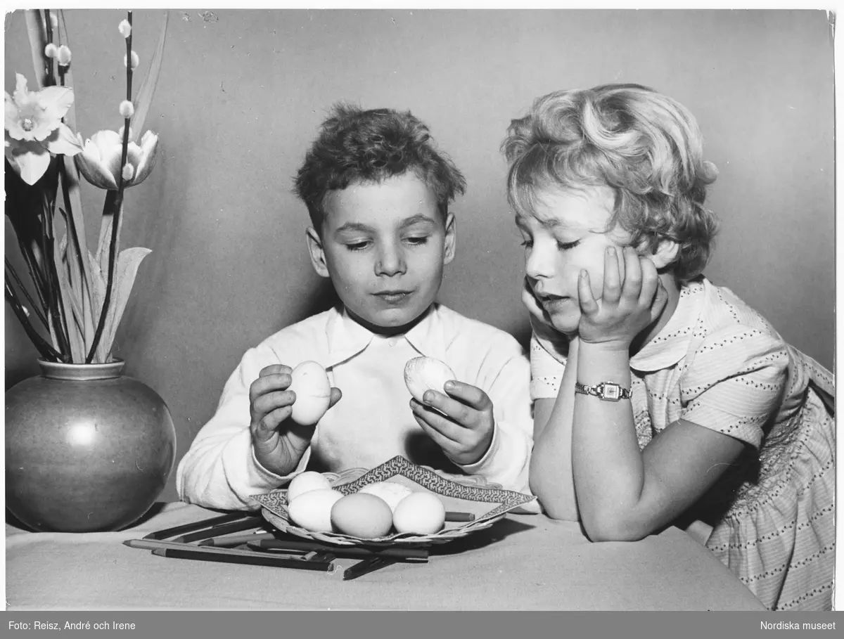 Två barn sitter vid bordet och tittar på påskägg.
