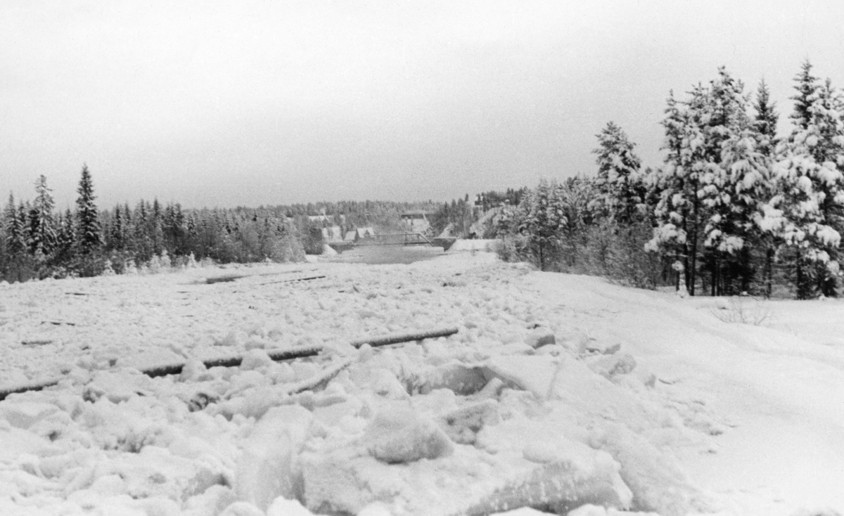 Isgang i elva Søndre Osa i Åmot (Hedmark) vinteren 1942.  Fotografiet er tatt fra en posisjon nær nordre elvebredd med utsikt nedover mot brua for vegen mellom Rena og Deset.  I forgrunnen har strømmen pakket sammen isflak, som til dels har reist seg slik at de danner ei meget ujevn overflate. Mellom isflakene lå det enkelte tømmerstokker.  Langs den nordre elvebredden (til høyre) later det til å ha vært en liten voll, som her var snødekt med en langsgående sti.  Til høyre for dette, og til venstre for den søndre bredden (til venstre), sto den snødekte barskogen tett.  Lengre nede i løpet skimter vi altså ei vegbru, et støpejernsspenn mellom to murte steinkar.  I området like ovenfor brua steg det opp litt damp, noe som tyder på at elveløpet var åpent der nede. 