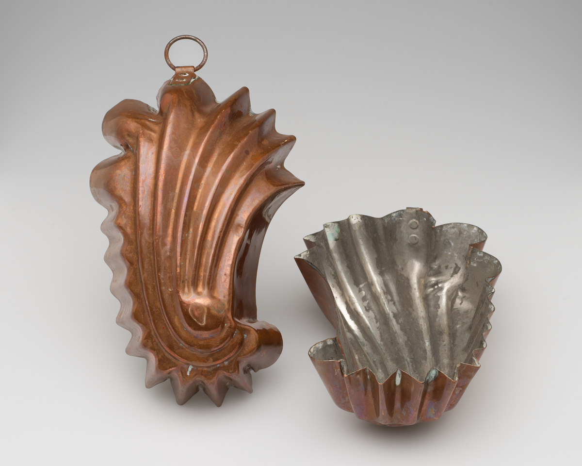 To skjellformede kakeformer av kobber. Innvending belagt med sølvfarget metall. Opphengsring i toppen av formen.