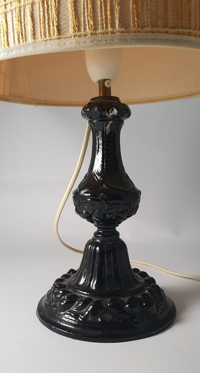 Elektrisk lampe med støpt fot fra Mandals Værksted, et støperi på Sanden i Mandal. Lampeføttene ble produsert for Mandal Paraffin Olie Co. på Risøbank ved Mandal. Parafinoljefabrikken var virksom fra 1862 til 1872.