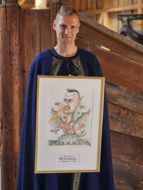 Årets Mesterborger 2023, Helge Larsen, mann i blå kappe med karikaturtegning av seg selv.