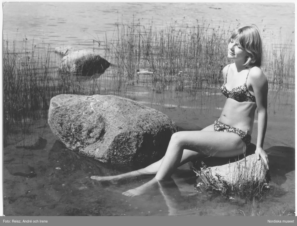 En flicka i badkläder sitter på en sten i vattnet på Öland.