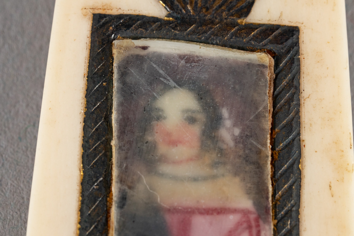 Hele brevåpneren er laget av bein med innfelt dekor, et portrett av en dame med et glass over. Øverst på skaftet er det tre røde perler. En mangler. Skaftet og knivbladet er føyd sammen og festet med to bein nagler