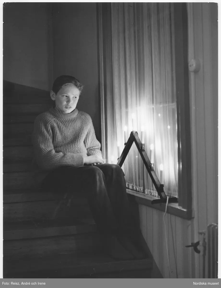 En pojke sitter i en trappa vid fönstret med adventsljusstake och tittar ut.