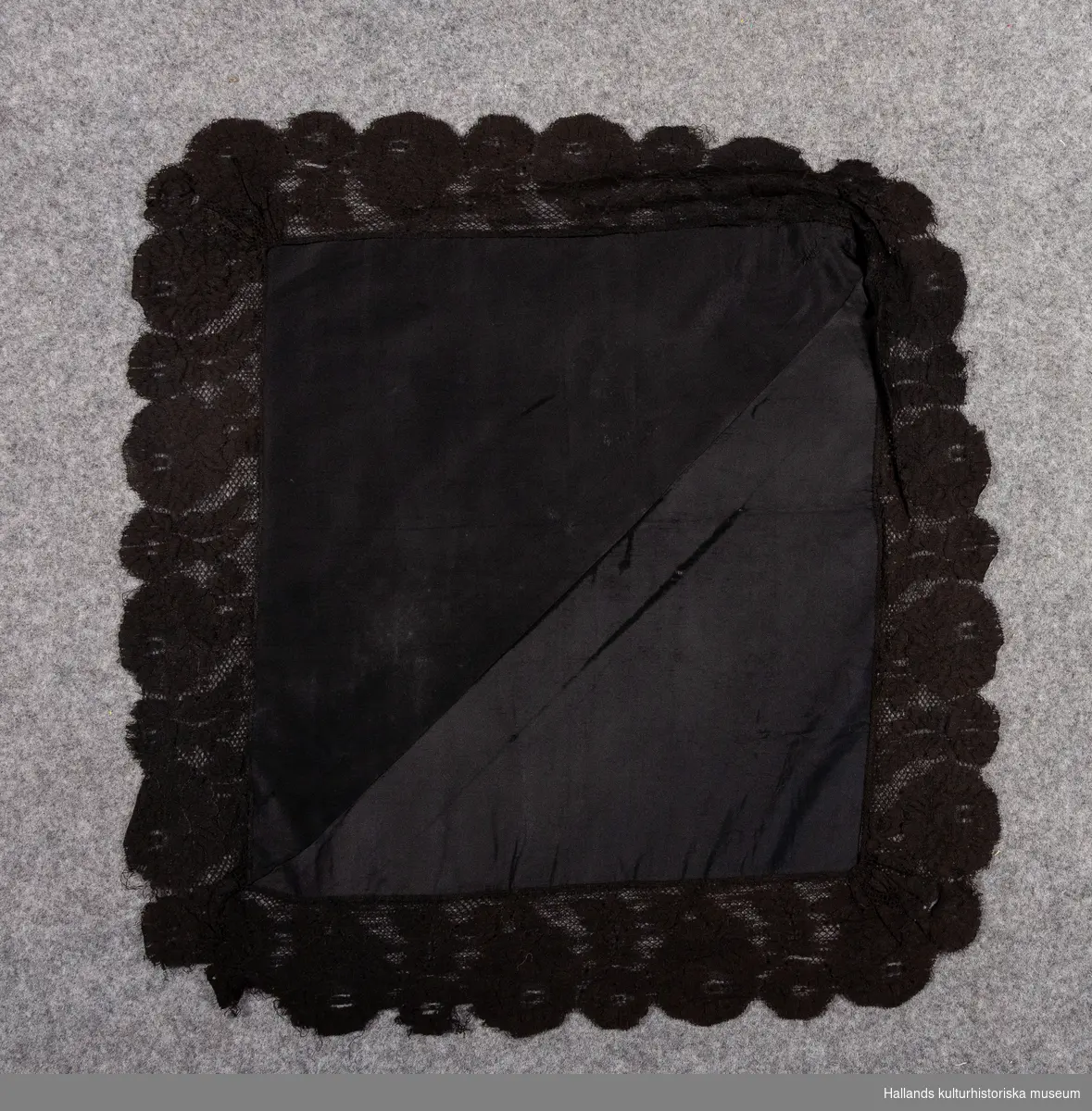 Svart sidensjal, huvudduk av slätvävd rips ihopsydd av två trekantiga bitar. Kantad med bred svart silkesspets.