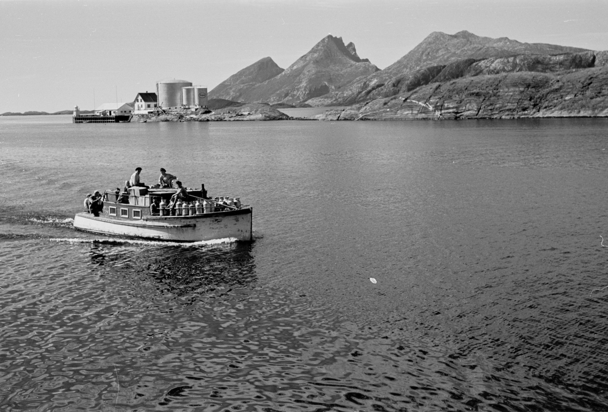 Alstahaug, Sandnessjøen. Båten "Vesla er ferdig lastet og er på vei til Leirfjord med gods, melkespann og folk. Båten fraktet folk, gods, varer og melkespann mellom Sandnessjøen og Leirfjord. Dønna sees i bakgrunnen.
