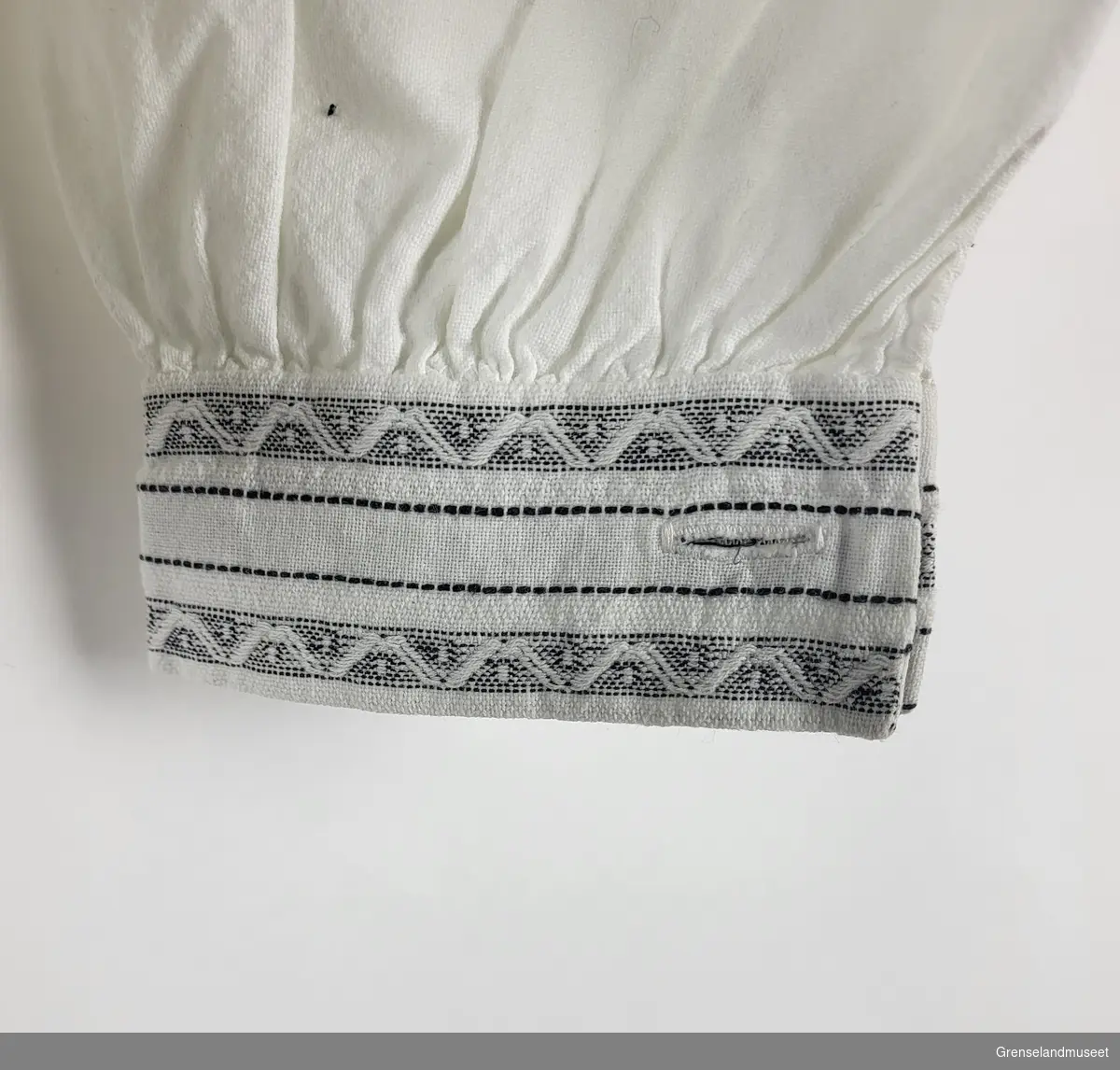 Gjenstandene er en hvit skjorte som har vært i bruk av Bjørnevatn Pikekor. Kragen og ermene er dekorert med sydd mønstersøm i hvitt og svart.
