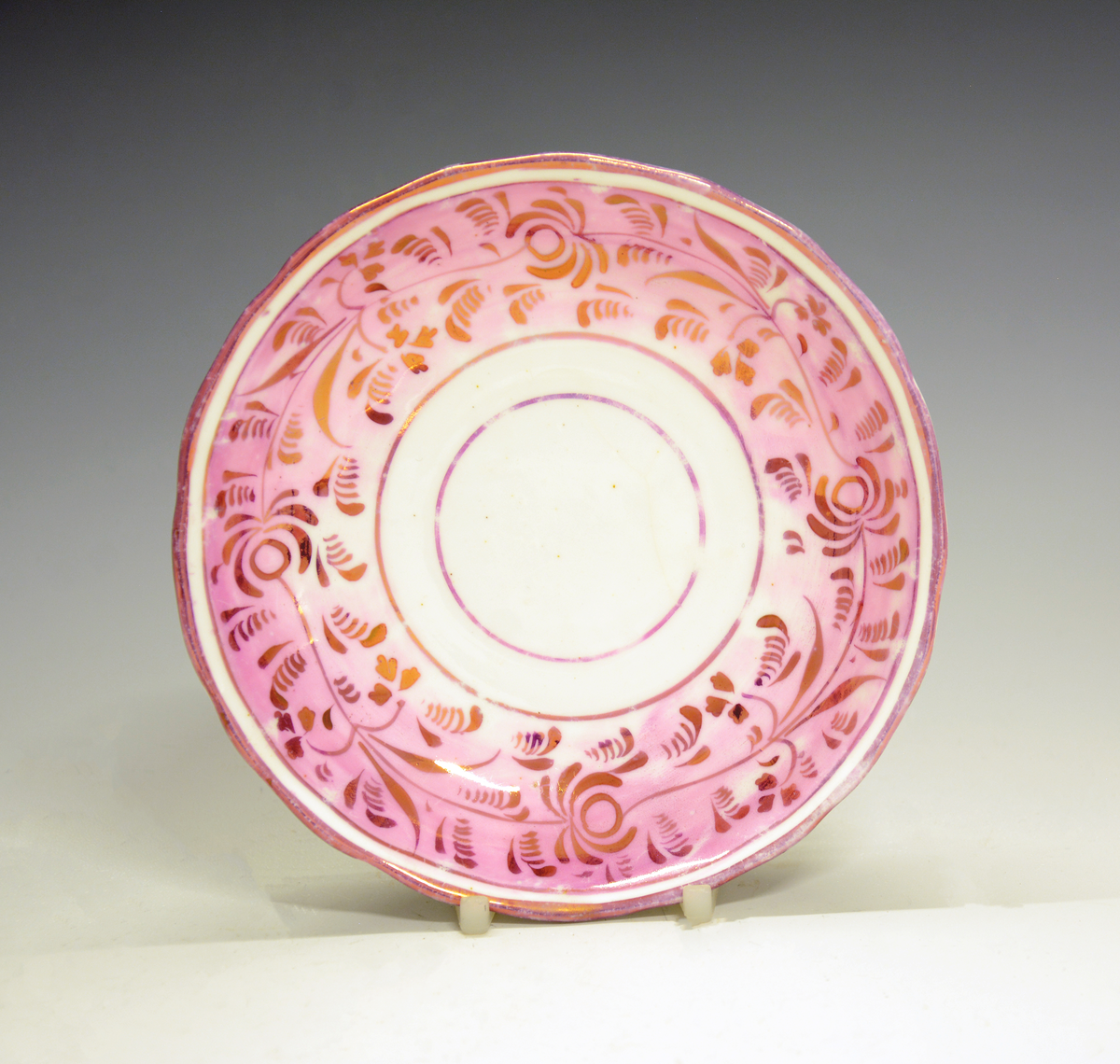 Fra protokollen: Tekopp med skål. Dekor i form av en frise med lys rød bunnfarge og påmalte blomsterranker i gull. Uten merke. Engelsk luster-keramikk  (lustreware/lusterware).