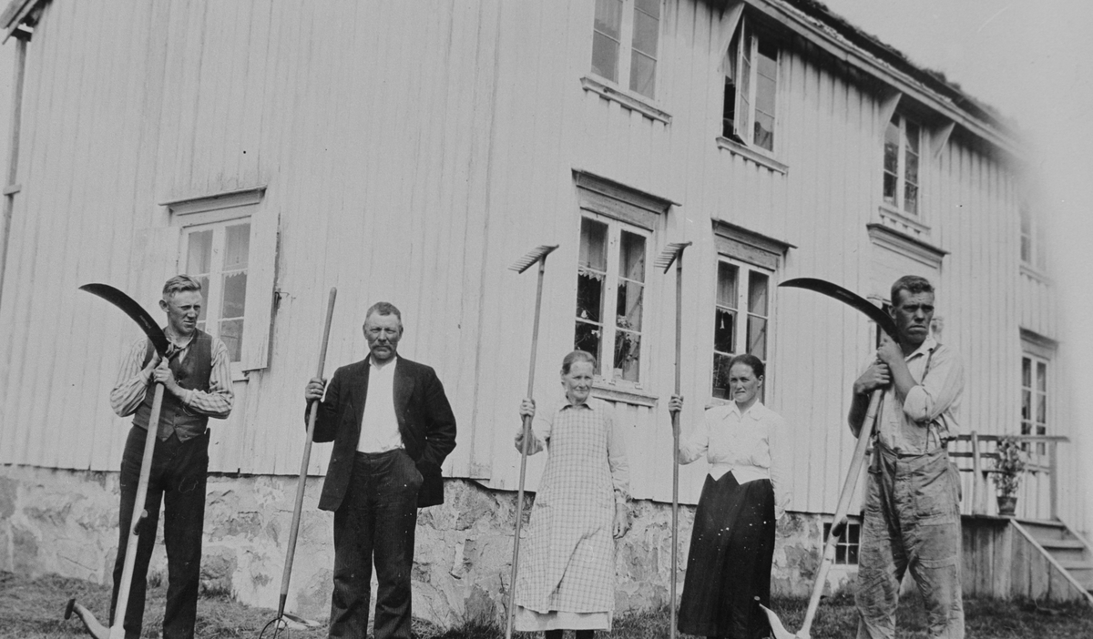 En pause i slåttonna på Børøya, Hitra. Mennesker oppstillt foran et hus.