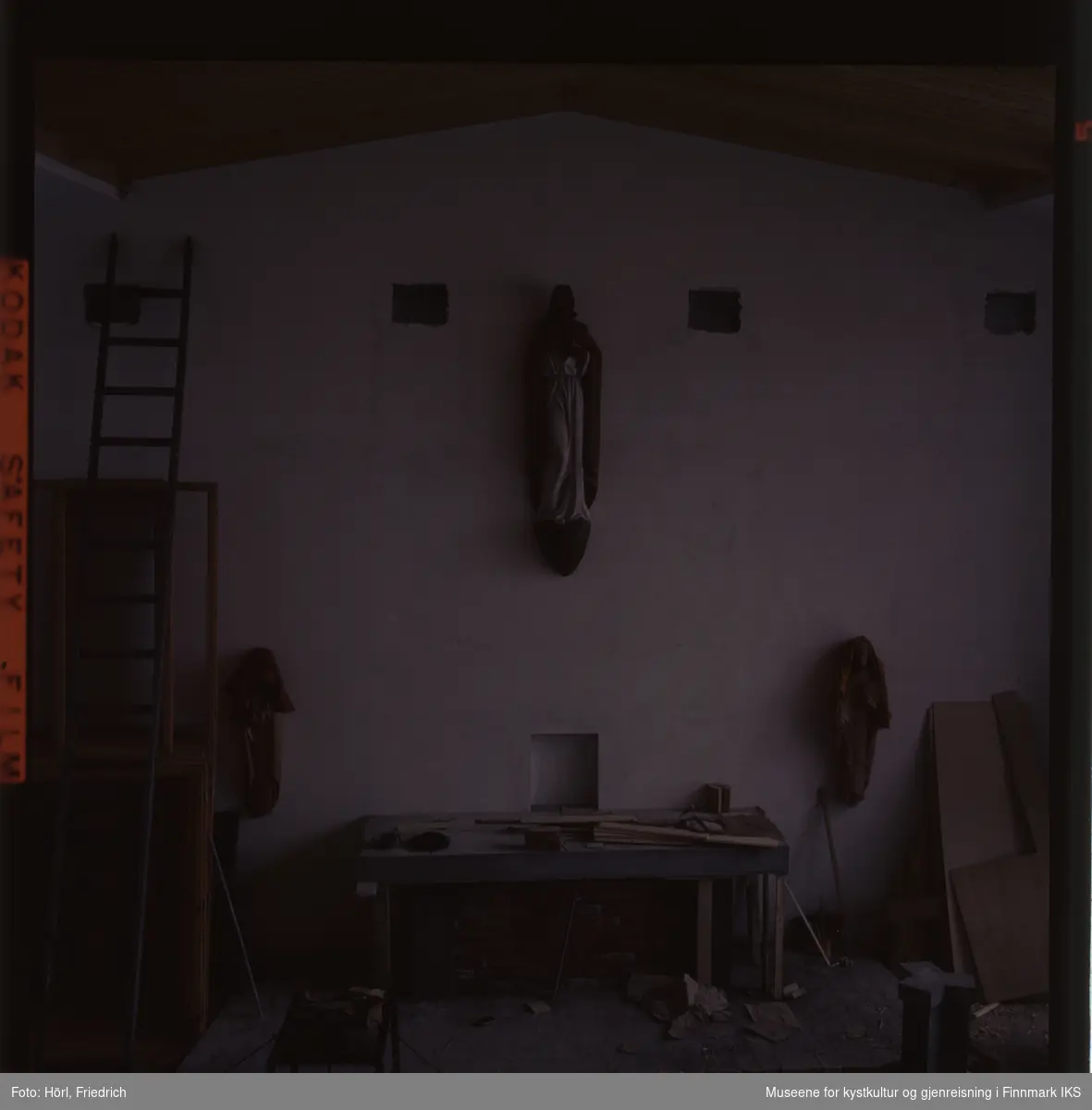 Fotografiet er noe underbelyst. Den viser interiøret av Den katolske kirke St. Mikael i Hammerfest i byggeperioden. Alteret er under byggingen. Skulpturene på veggen til venstre og høyre for det er dekket med tepper. Til venstre i bildet skimter man en lang stige som er lent mot veggen.